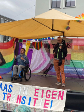 Jochem (zittend in rolstoel, tolkend) en vreer (staand) bij presentatie rapport Trans* zorg Anders
